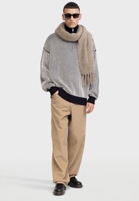 Pulover supradimensionat cu dungi negre și albe, cu manșete negre, pantaloni din corduroy bej și o eșarfă lungă de culoare maronie deschisă. Ochelari de soare negri și pantofi negri.