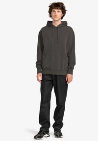 Dark gray hoodie with a front pocket, drawstring hood, and ribbed cuffs; paired with black denim pants and black athletic shoes.