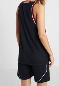 Débardeur de sport noir avec encolure rayée rouge et blanche, associé à un short noir avec des accents blancs sur les côtés. Texture en mesh visible.