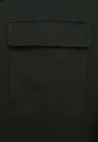 Dark green shirt featuring a square chest pocket with a rounded flap, made from soft fabric with a smooth texture.