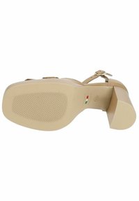 Sandale à talons hauts beige avec une semelle en caoutchouc texturé, une sangle à boucle et un large petit talon, présentant un cuir lisse et un design minimaliste.