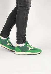 Zelené semišové a kožené tenisky s krémovými akcentmi, textúrovaný vrch, okrúly špička, hrubá čierna podrážka a kontrastné biele šnúrky.