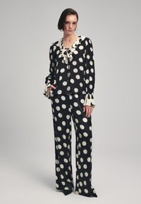 Blusa a pois bianco e nero con scollatura e polsini arricciati, abbinata a pantaloni larghi coordinati. Tessuto morbido e fluente.