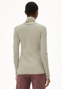 Maglietta a maniche lunghe con collo alto in tessuto grigio chiaro, caratterizzata da un design aderente e da una texture morbida, abbinata a pantaloni bordeaux sbiaditi.