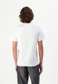 White short-sleeve t-shirt in cotton, featuring a crew neck and a relaxed fit, worn with dark gray jeans. Back view shows smooth texture.