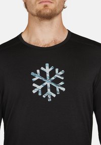 Långärmad svart skjorta i lättviktsmaterial med en stor snöflinge-grafik i blå accenter på framsidan.