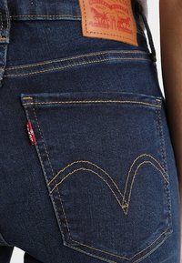 Mörkblå denimjeans har en läderetikett, gul stickning och en ikonisk bakfickdesign med ett subtilt böjt mönster.