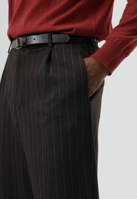 Zwarte broek met krijtstreep en een getailleerde pasvorm, voorzien van steekzakken aan de voorkant en een gestructureerde zwarte leren riem. Rode top met lange mouwen maakt de look af.