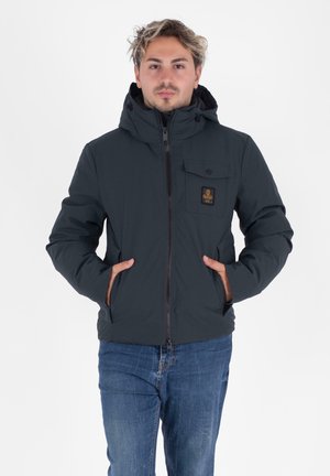 Giacca scura e isolata con cappuccio, chiusura con zip e tasca sul petto anteriore. Il materiale è liscio, con accenti marroni vicino alle tasche.