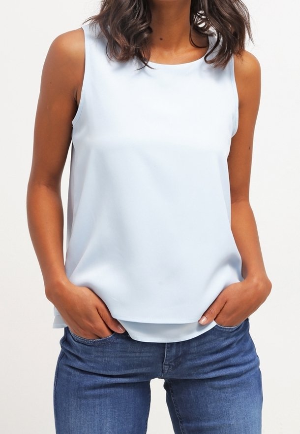 Haut sans manches bleu clair en tissu lisse ; encolure ronde ; coupe ample ; ourlet superposé ; porté avec un jean bleu.