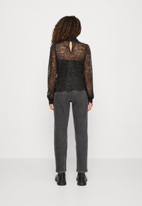 Blouse en dentelle noire avec un dos en forme de trou, manches longues et ourlet festonné, associée à un jean gris fuselé et des bottines noires.