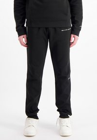 Zwarte sportbroeken met een getailleerde pasvorm, gemaakt van een gladde stof. Bevat witte logo-accenten en zijstrepen, gecombineerd met witte sneakers.