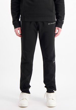 Zwarte sportbroeken met een getailleerde pasvorm, gemaakt van een gladde stof. Bevat witte logo-accenten en zijstrepen, gecombineerd met witte sneakers.