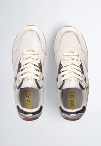 Sneaker beige e marroni con accenti testurizzati, dotati di occhielli dorati, lacci piatti e un pannello laterale decorato; linguetta e colletto imbottiti.