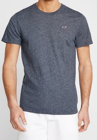 Camiseta de algodón azul marino jaspeada con mangas cortas, cuello redondo y un pequeño logo en el lado izquierdo del pecho. Textura suave, corte regular.