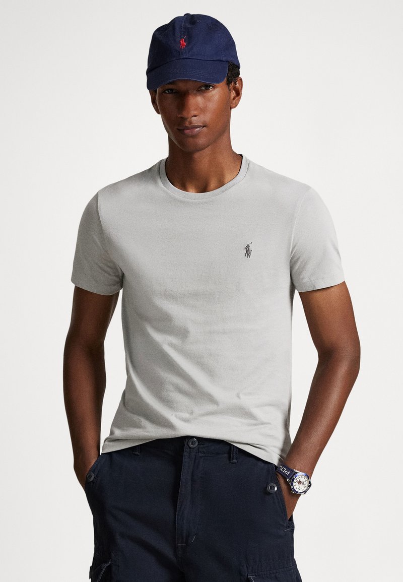 Ανοιχτό γκρι βαμβακερό T-shirt με στρογγυλή λαιμόκο�ψη και μικρό κεντητό λογότυπο. Συνδυασμένο με ναυτικό μπλε καπέλο και ναυτικά μπλε cargo σορτς. Λεπτομέρειες casual εμφάνισης εμφανείς.