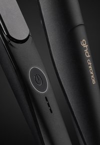 Un lisseur de cheveux noir au design élégant, avec un bouton d'alimentation rond, un profil mince, et le logo "ghd chronos" en doré.