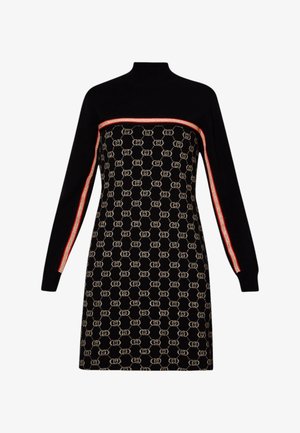 Femme portant une robe noire à manches longues à motifs avec un détail d'une rayure rouge, associée à des bottes noires texturées à talons montant jusqu'aux genoux.