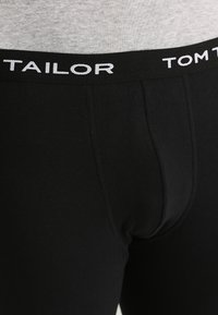 Boxer ajustados de algodón negro con una suave cintura elástica que presenta letras blancas que dicen "TAILOR" y "TOM" en mayúsculas.