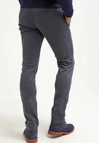 Grijze slim-fit broek van gladde stof, voorzien van achterzakken, subtiele stiknaden, en gecombineerd met marineblauwe suède enkellaarsjes.
