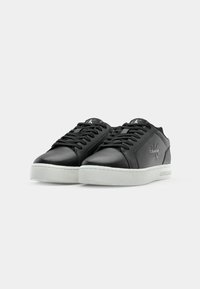 Zwarte synthetische sneakers met een gladde afwerking, witte rubberen zool, ronde neus en een logo op de zijkant en de tong.