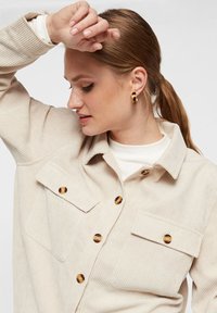 Beige Kordhemdjacke mit zwei Brusttaschen, goldfarbenen Knöpfen und Kragen. Verfügt über eine gerippte Textur und eine lockere Passform.