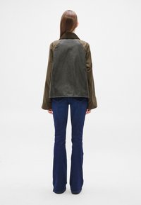 Olive green and dark gray jacket with a collar, raglan sleeves, and a relaxed fit, paired with flared blue jeans.