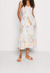 Květinové midi šaty ve světle modré barvě. Mají volánkové ramínka, přiléhavý korzet, boční kapsy a plnou sukni s pastelovými květinovými vzory.