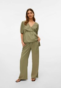 Haut texturé vert olive avec un décolleté plongeant et une taille froncée, associé à un pantalon large et ample. Des tongs simples.