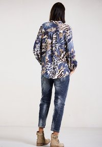 Langärmlige Blumenbluse in Blau und Beige, kombiniert mit verwaschenen blauen Jeans. Beigefarbene Ankle-Boots mit Riemen runden den Look ab.