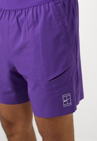 Lila Sportshorts aus leichtem Stoff, mit einer Reißverschlusstasche und einem weißen Nike-Logo am Saum. Elastischer Bund für zusätzlichen Komfort.