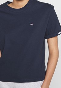 Mörkblå bomulls t-shirt med rund halsringning, korta uppvikta ärmar och en liten logotyp på bröstet. Mjuk, slät textur.