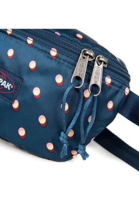 Sac en nylon bleu avec des pois roses et jaunes, double zipper argenté et bandoulière en tissu. Surface texturée avec des accents cousus.