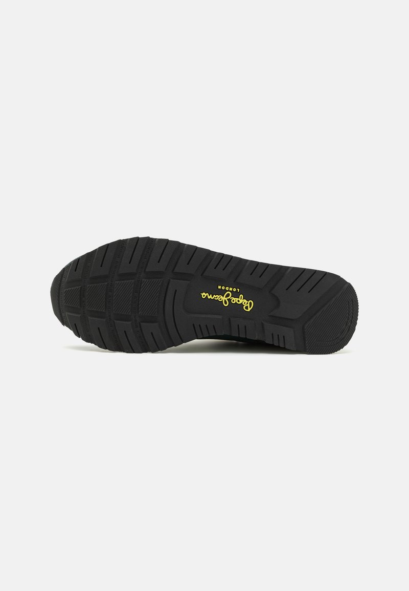 Suela de zapato de goma negra con un patrón texturizado para tracción. Presenta un logo amarillo en el lado, diseñado para la durabilidad y el agarre.