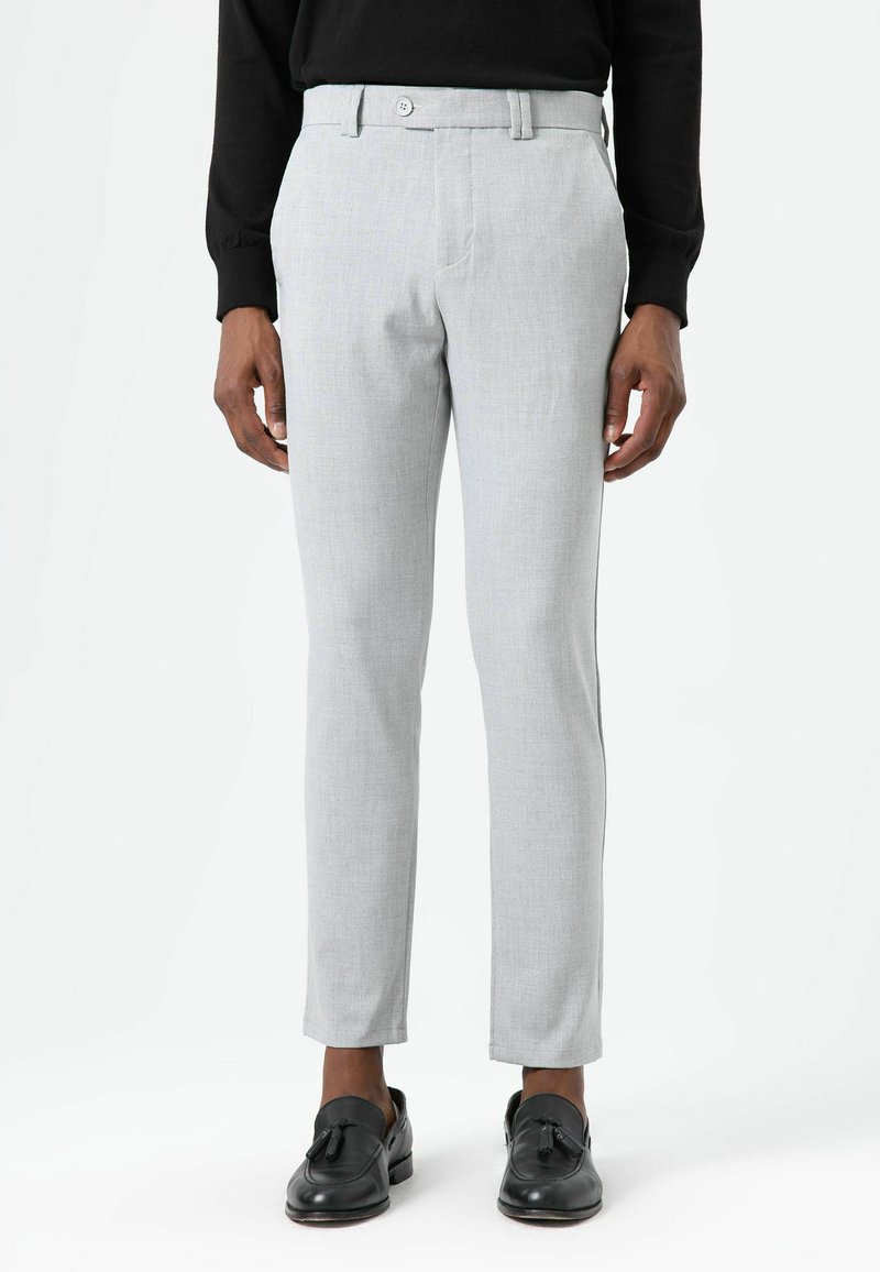 Lichtgrijze, op maat gemaakte broek met een gladde textuur, voorzien van een platte voorkant en twee voorzakken, gecombineerd met zwarte instapschoenen.