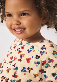 Cotton t-shirt with a rounded neckline, featuring a beige base and a multicolored floral pattern in red, blue, green, and brown.