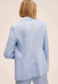 Giacca in lino azzurro chiaro con taglio classico, rever a punte e spacco posteriore singolo. Il tessuto testurizzato offre un aspetto casual ma curato.
