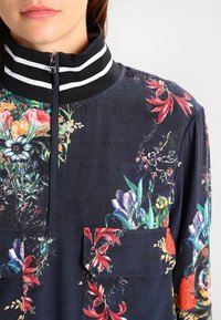 Koszula z długim rękawem w ciemne kwiaty z wysokim kołnierzem w czarno-białe paski; zawiera kieszenie z przodu oraz różnorodne kolorowe wzory kwiatowe.