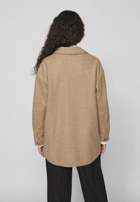 Cappotto corto in misto lana beige con colletto, maniche lunghe e polsini con bottone. Presenta un orlo arrotondato e una vestibilità comoda.