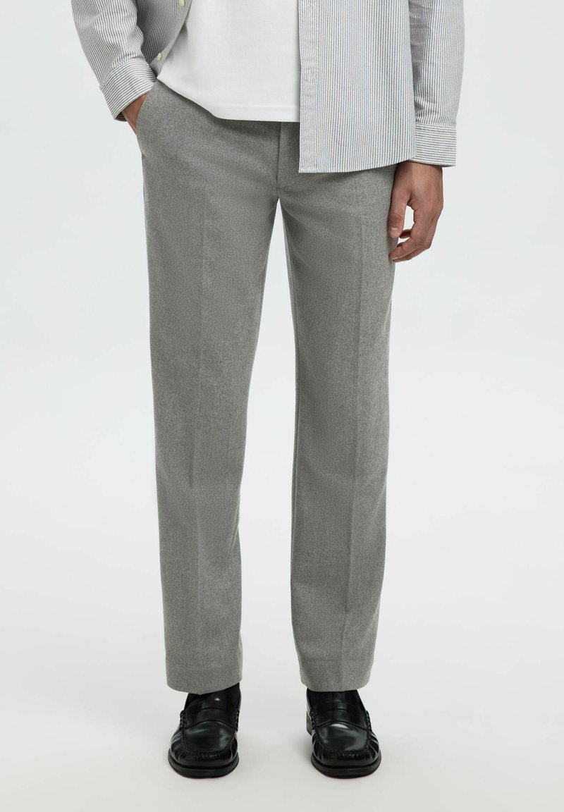 Pantaloni grigi chiari, testurizzati, con una vestibilità dritta, caratterizzati da una finitura liscia e linee pulite. Abbinati a scarpe nere per un contrasto.