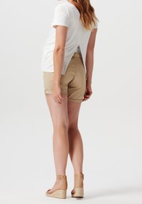 Camicia bianca a maniche corte con spacco sul retro, abbinata a pantaloni corti color sabbia fino al ginocchio e zeppe in espadrillas color sabbia. Design semplice e tessuto leggero.