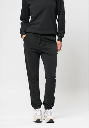 Sorte sweatpants med elastisk talje og manchetter ved anklerne, der har en afslappet pasform og sidelommer. Bæres med grå og hvide sneakers.