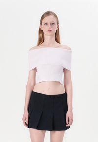 Off-shoulder, geribbelde crop top in lichtroze, gecombineerd met een zwarte geplooide mini-jurk met een gladde textuur en strakke lijnen.