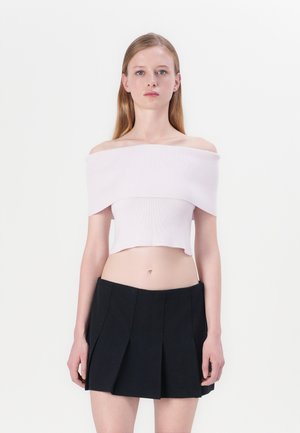 Off-shoulder, geribbelde crop top in lichtroze, gecombineerd met een zwarte geplooide mini-jurk met een gladde textuur en strakke lijnen.