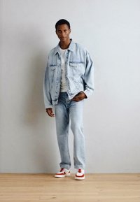 Denimjakke med store frontlommer, lys vask, sammen med en hvit t-skjorte og lyseblå jeans. Fottøyet har røde detaljer.