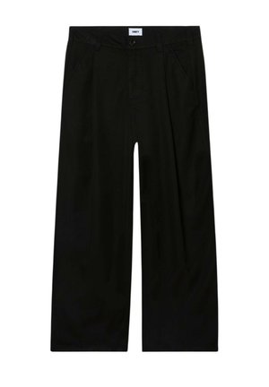 Schwarze Hose mit weitem Bein, seitlichen Taschen, Gürtelschlaufen, Knopfverschluss und einem sichtbaren weißen Etikett mit der Aufschrift „OBEY“ am Bund.