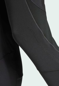 Schwarzes sportliches Langarmoberteil aus glattem Stoff mit strukturierten Akzenten und lasergeschnittenen Belüftungslöchern an den Ärmeln und Seiten.