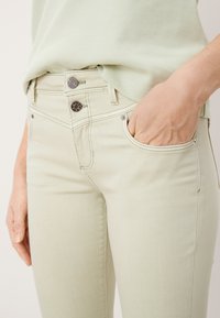 Jasnozielone dżinsy o slim fit, z tylnymi kieszeniami, srebrnymi akcentami i kontrastowym przeszyciem. Gładka faktura, casualowy styl.