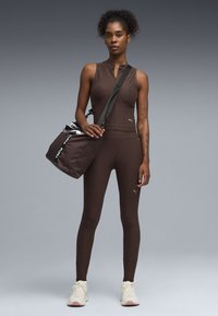 Καφέ αθλητικό τοπ και κολάν από υφασμάτινη υφή, συνδυασμένα με καφέ τσάντα με διακοσμητικό λουρί και λευκά λογότυπα.