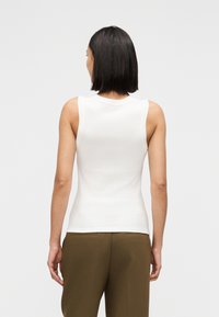 Λευκό αμάνικο τοπ με στρογγυλή λαιμόκοψη, εφαρμοστή γραμμή και ομαλή υφή, συνδυασμένο με χακί πράσινο παντελόνι.